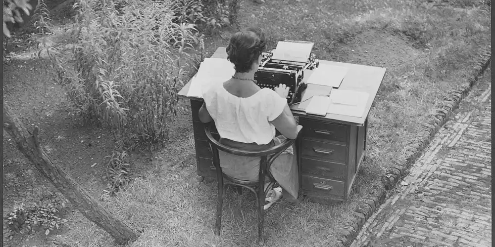 Typiste aan een bureau met schrijfmachine, buiten op het gras